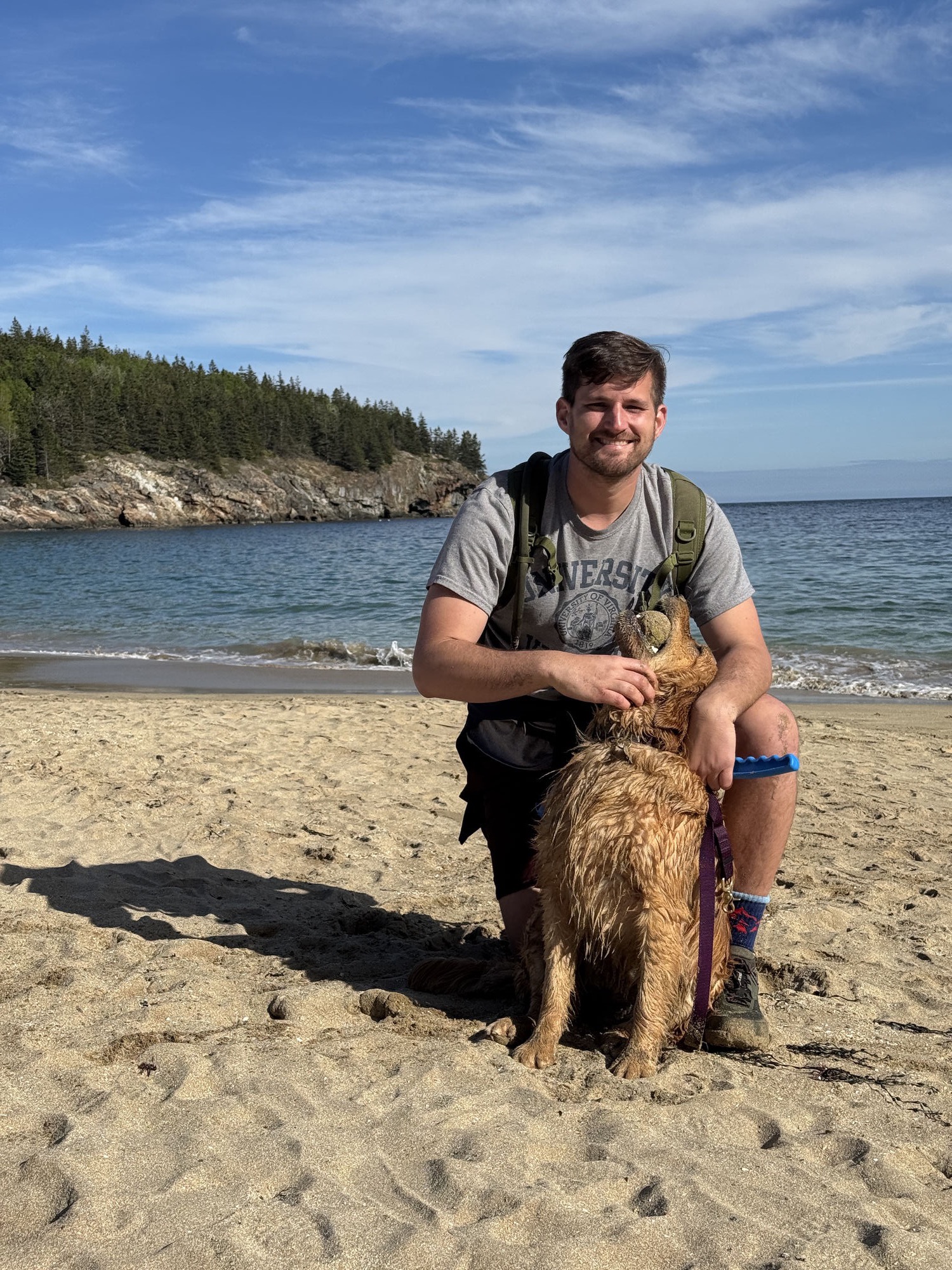 Justin Gregoire with his golden retriever on a beach in Acadia